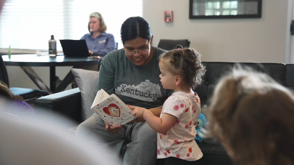 A parenting adult and child are looking at a board book during a Play with Purpose playgroup session.