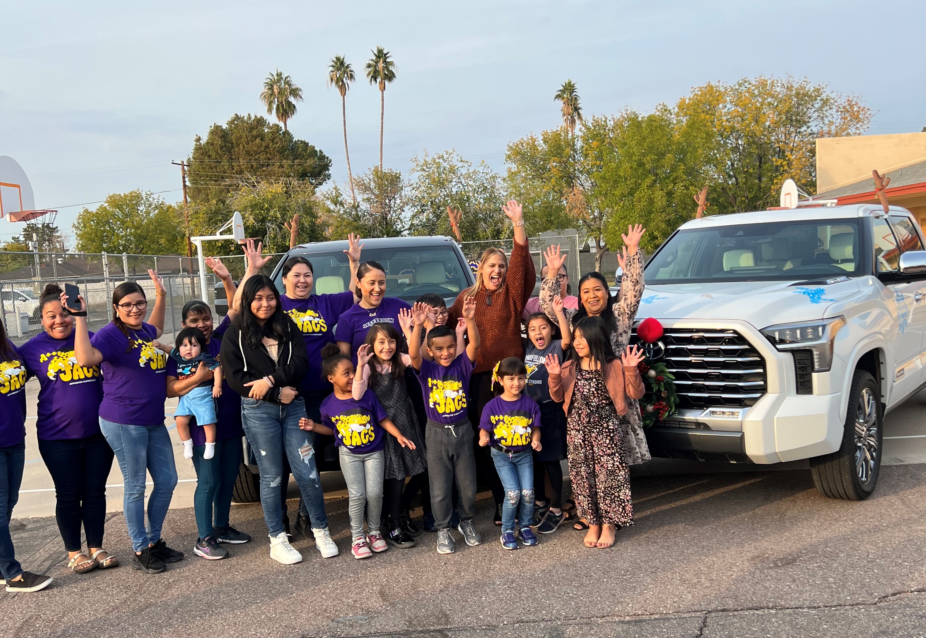 Ivonne Ortiz and a group of students and families pose enthusiastically in front of two Toyota Tundras with school supplies.